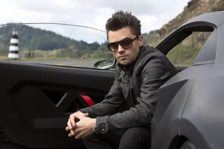 Dominic Cooper poses in a stylish outfit beside a sleek car, capturing a moment from the movie Need For Speed. This HD wallpaper showcases a thrilling blend of action and attitude.