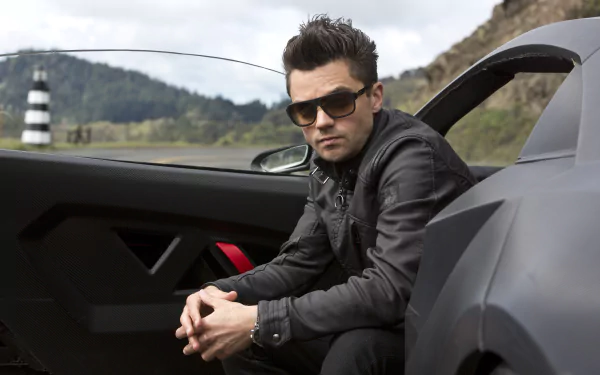 Dominic Cooper poses in a stylish outfit beside a sleek car, capturing a moment from the movie Need For Speed. This HD wallpaper showcases a thrilling blend of action and attitude.