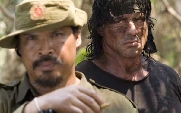 HD desktop wallpaper showing a scene from the movie Rambo with a soldier in focus and another character in the background, both displaying intense expressions.