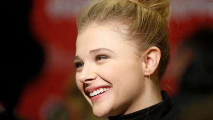 HD desktop wallpaper featuring a close-up of celebrity Chloë Grace Moretz smiling with her hair tied up against a blurred background.