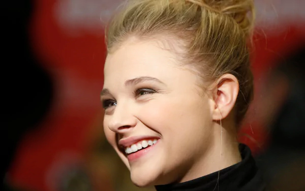 HD desktop wallpaper featuring a close-up of celebrity Chloë Grace Moretz smiling with her hair tied up against a blurred background.