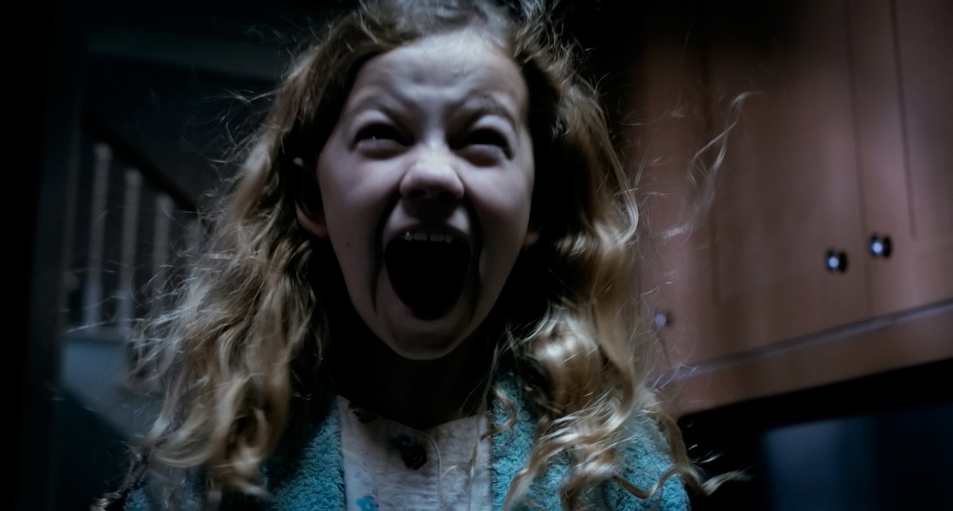 A high-definition wallpaper featuring Megan Charpentier in a chilling scene from the movie Mama, capturing intense emotion with her screaming expression against a dark background.