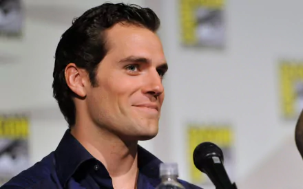 HD desktop wallpaper featuring British actor and celebrity Henry Cavill smiling at a microphone during a public event.