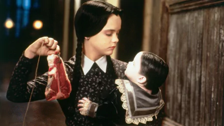 Christina Ricci as Wednesday Addams holds a piece of meat while gazing at a doll in this iconic scene from *Addams Family Values*, featured as a striking HD desktop wallpaper.