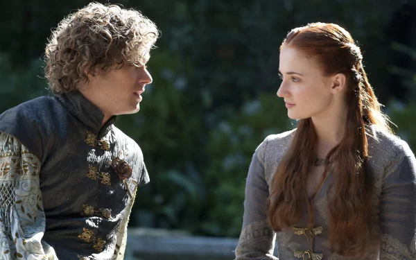 2K Quad HD PC wallpaper: two TV actors in medieval costumes — a curly blond man in an ornate doublet converses with a red‑haired braided woman in a grey gown outdoors.