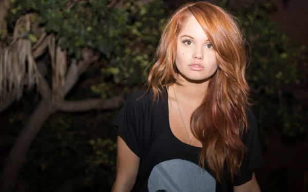 Close-up portrait of a redheaded woman in a black tee against dark foliage — 5K Ultra HD PC desktop wallpaper.