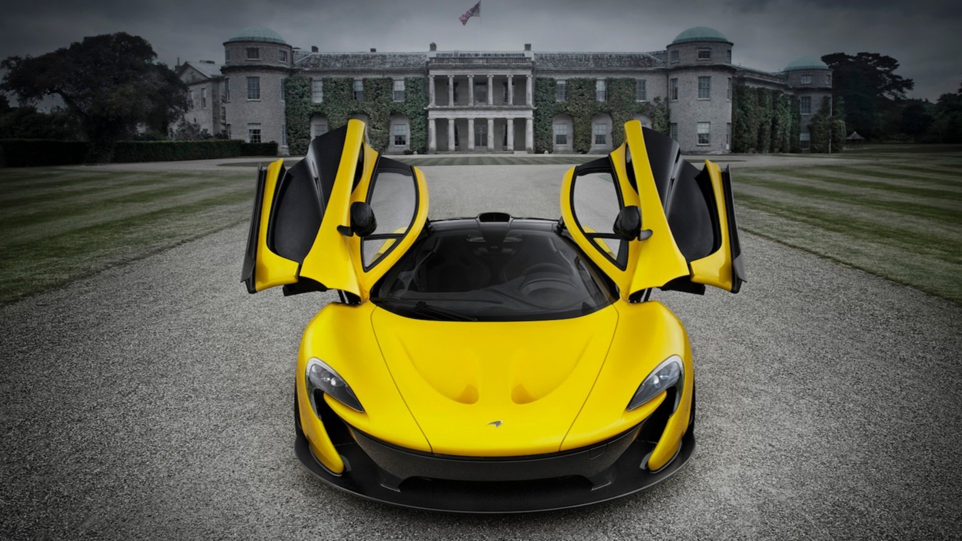 HD desktop wallpaper featuring a bright yellow McLaren P1 with its doors raised, parked on a gravel driveway in front of a grand historic mansion.