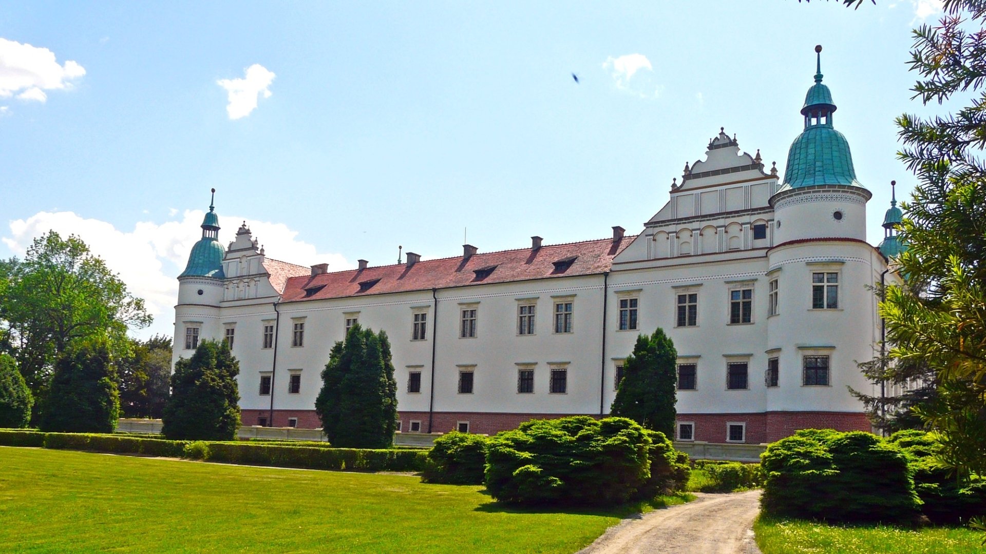 HD desktop wallpaper featuring the Baranów Sandomierski Castle, a historic man-made structure surrounded by greenery under a clear blue sky.