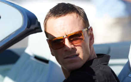 Close-up of an actor in sunglasses in a convertible, glancing back; cinematic still from the movie The Counselor used as a 2K Quad HD PC desktop wallpaper.