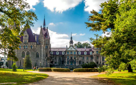 HD desktop wallpaper showcasing Moszna Castle, a striking man-made historic building surrounded by lush greenery under a partly cloudy sky.