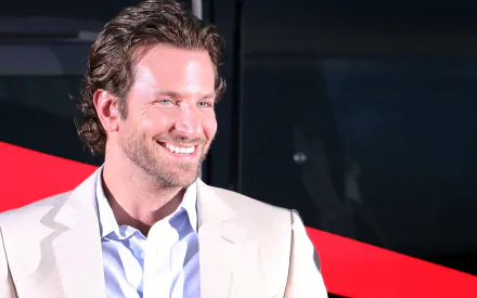 HD desktop wallpaper featuring American actor and celebrity Bradley Cooper smiling against a dark background with a red diagonal accent.