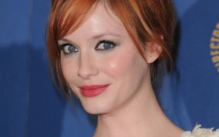 HD desktop wallpaper featuring American actress and celebrity Christina Hendricks with red hair, blue eyes, and a soft smile against a blue background.
