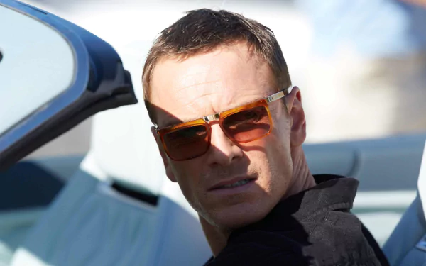 Close-up of an actor in sunglasses in a convertible, glancing back; cinematic still from the movie The Counselor used as a 2K Quad HD PC desktop wallpaper.