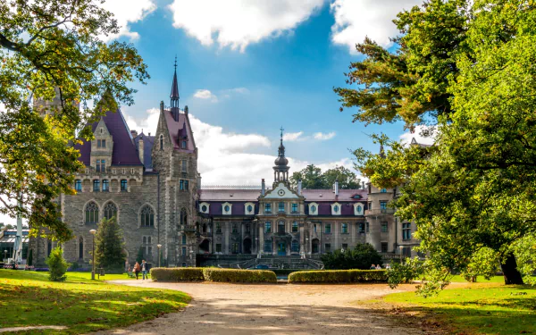HD desktop wallpaper showcasing Moszna Castle, a striking man-made historic building surrounded by lush greenery under a partly cloudy sky.