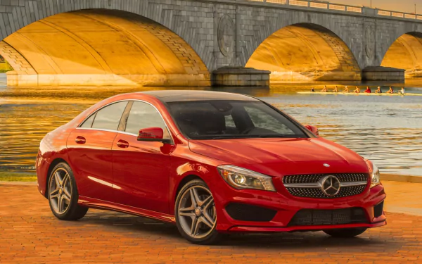 Red Mercedes-Benz CLA-Class parked on a riverside promenade at sunset, reflected in water beneath an arched stone bridge — HD PC desktop wallpaper and background.