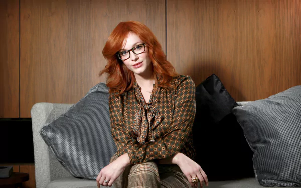 HD desktop wallpaper featuring American actress Christina Hendricks seated on a couch with wooden paneling in the background.