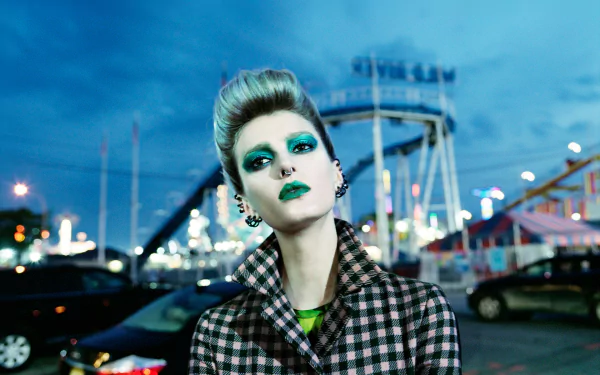 HD PC desktop wallpaper featuring French model Sigrid Agren with striking makeup and a checkered coat against a twilight urban backdrop.