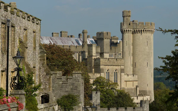 HD PC desktop wallpaper of man-made Arundel Castle: sunlit stone walls, battlements and round towers framed by trees beneath a pale blue sky.