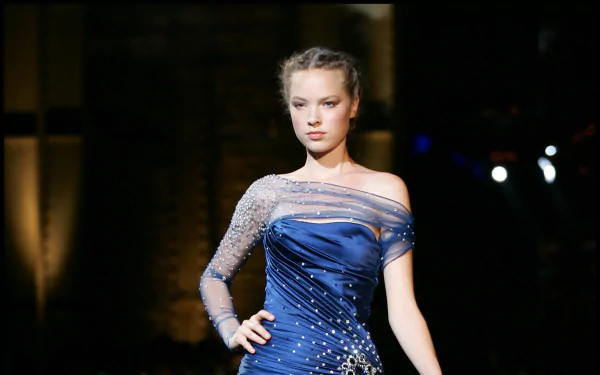 HD PC desktop wallpaper featuring French model Héloïse Guérin in an elegant, embellished blue gown on a dimly lit runway.