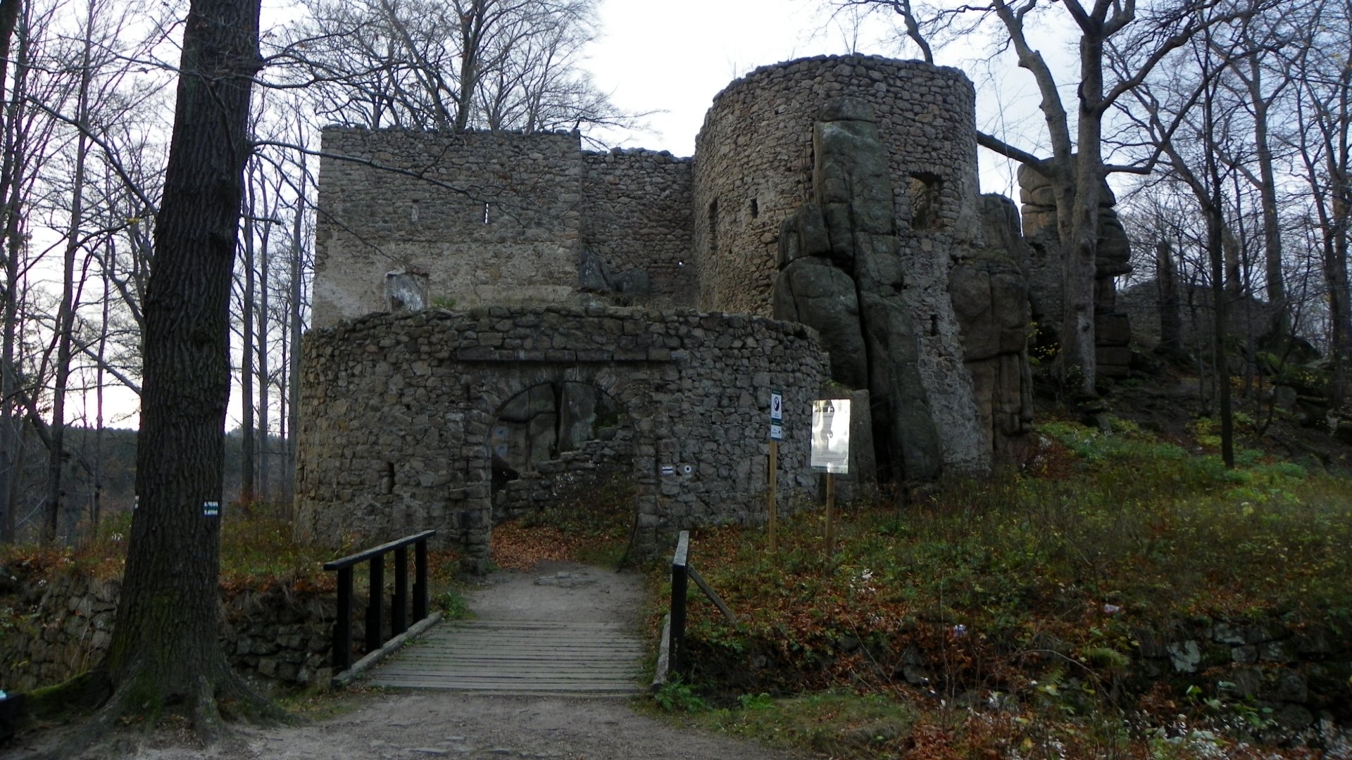 Bolczów Castle ruins framed by bare trees, a wooden footbridge leading to stone towers and rocky walls — man-made HD PC desktop wallpaper/background.