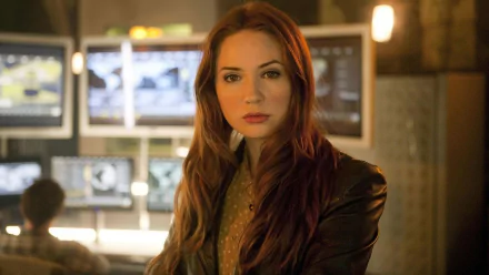 HD desktop wallpaper of Karen Gillan as Amy Pond from the TV show Doctor Who (2005), featuring her in a focused pose with blurred computer monitors in the background.