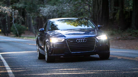 HD PC desktop wallpaper featuring a sleek black Audi A3 driving on a forested road with headlights on.