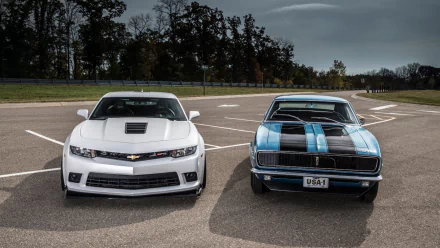 A Chevrolet Camaro Z28 stands prominently alongside a modern white Chevrolet Camaro, showcasing a blend of classic and contemporary automotive design.