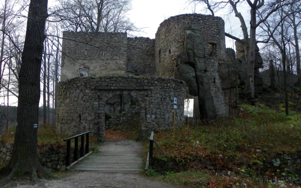 Bolczów Castle ruins framed by bare trees, a wooden footbridge leading to stone towers and rocky walls — man-made HD PC desktop wallpaper/background.