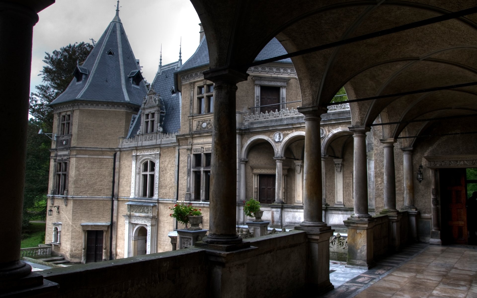 HD PC desktop wallpaper showing man-made Goluchów Castle from an arched stone gallery, ornate towers and wet walkway in soft daylight.