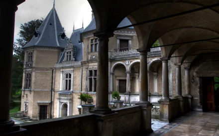 HD PC desktop wallpaper showing man-made Goluchów Castle from an arched stone gallery, ornate towers and wet walkway in soft daylight.