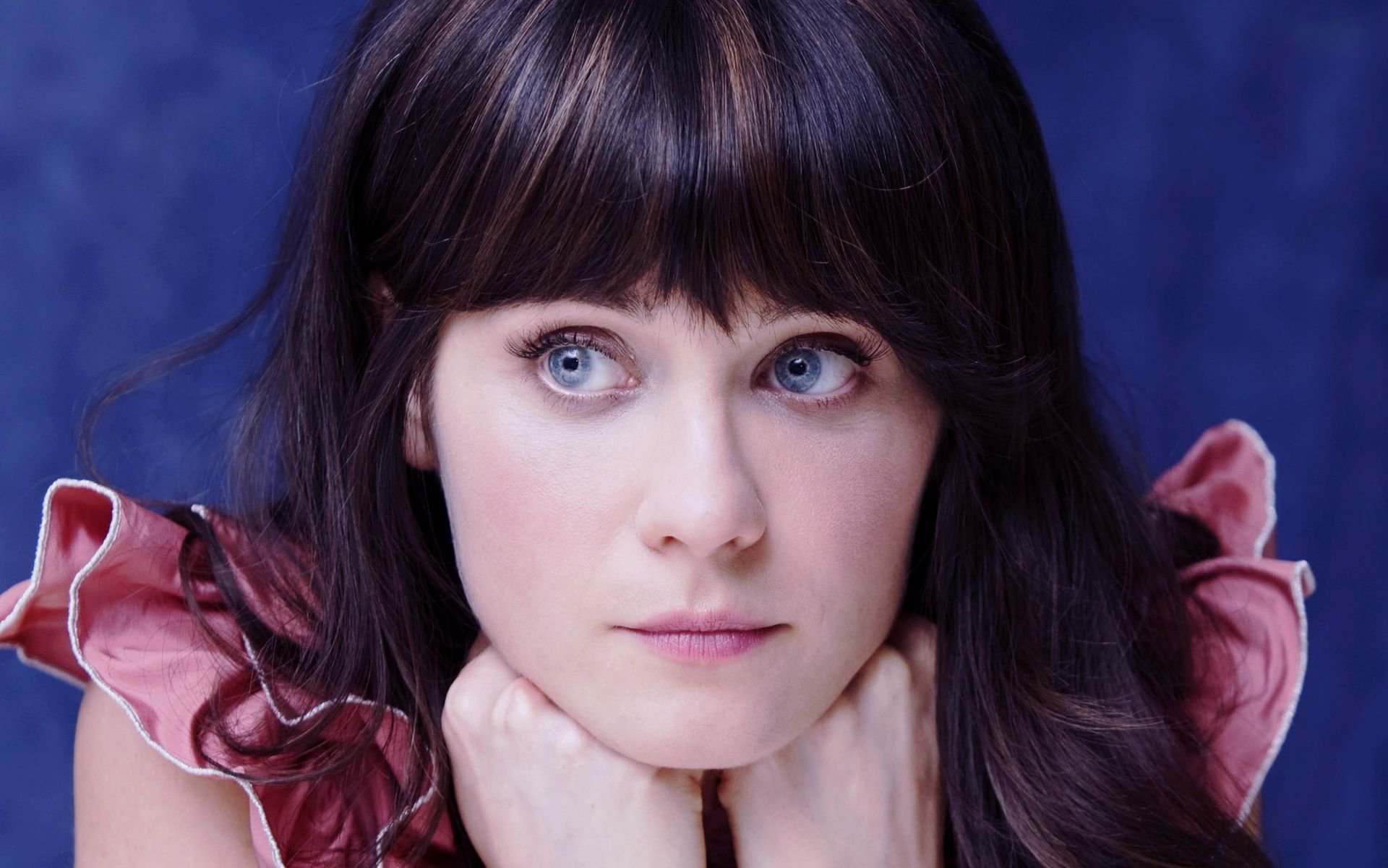 HD PC desktop wallpaper featuring a close-up portrait of celebrity Zooey Deschanel with dark hair, blue eyes, and a contemplative expression against a blue background.
