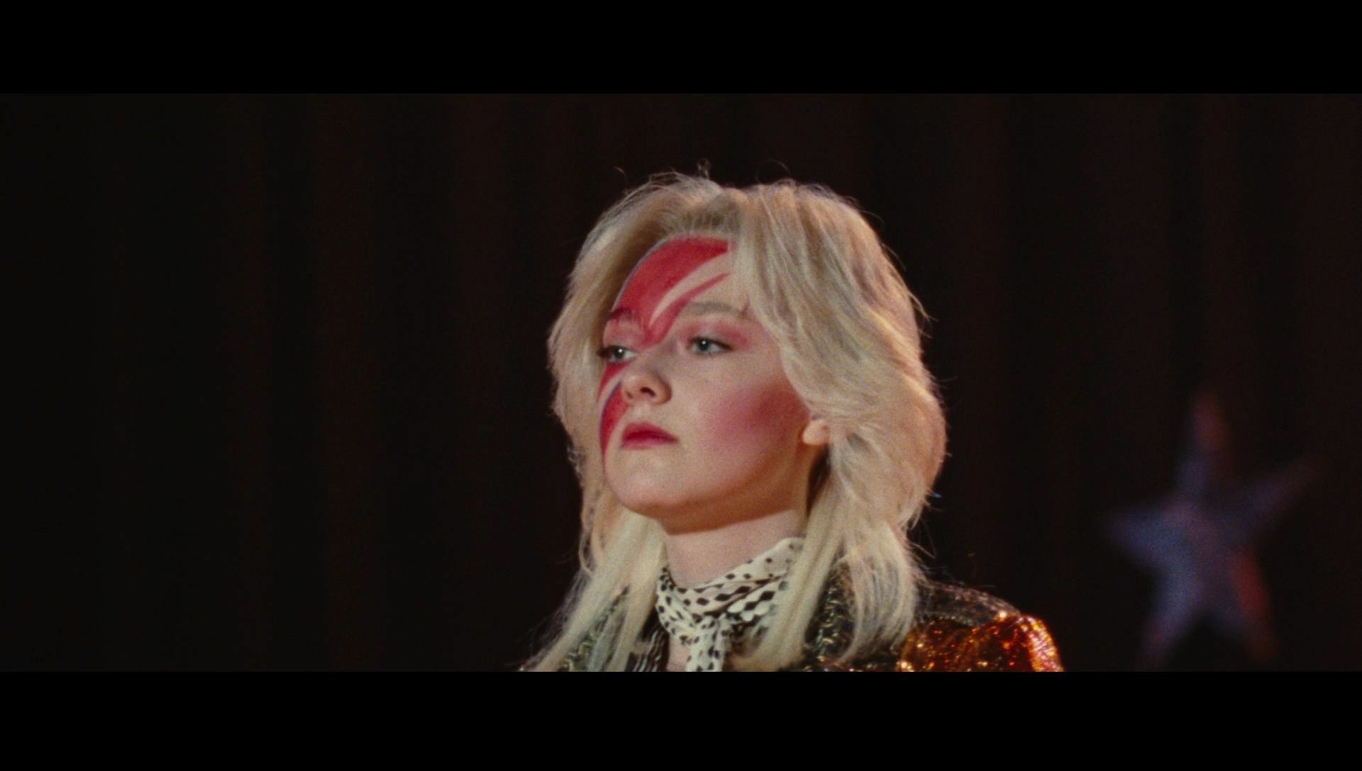 HD PC desktop wallpaper: movie still from The Runaways — a blonde performer with red lightning face paint and sequined jacket standing on a dark stage backdrop.