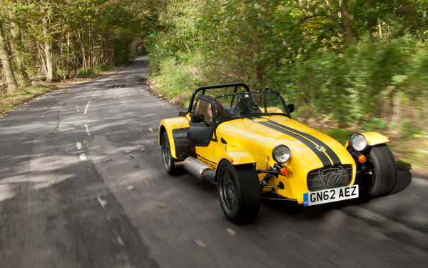 HD desktop wallpaper featuring a yellow Caterham Supersport R driving on a winding forest road, showcasing the vehicle’s sporty design and dynamic performance.