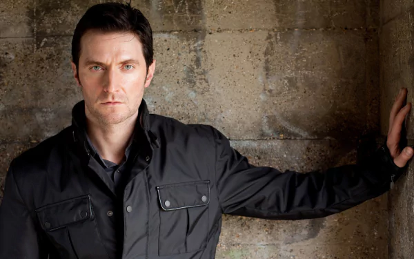 HD desktop wallpaper featuring English actor Richard Armitage posing against a textured stone wall.