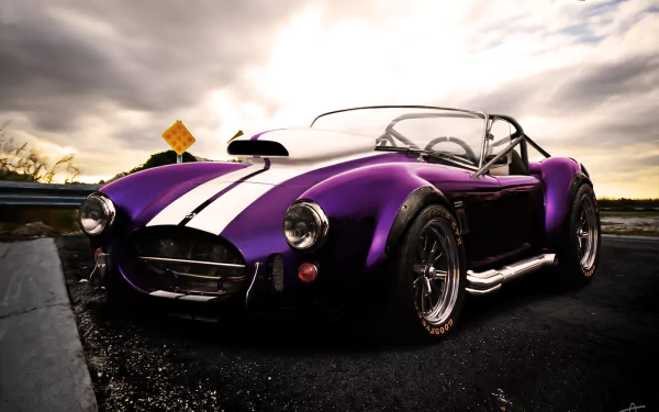 HD desktop wallpaper featuring a sleek purple AC Shelby Cobra with white racing stripes under a dramatic cloudy sky.