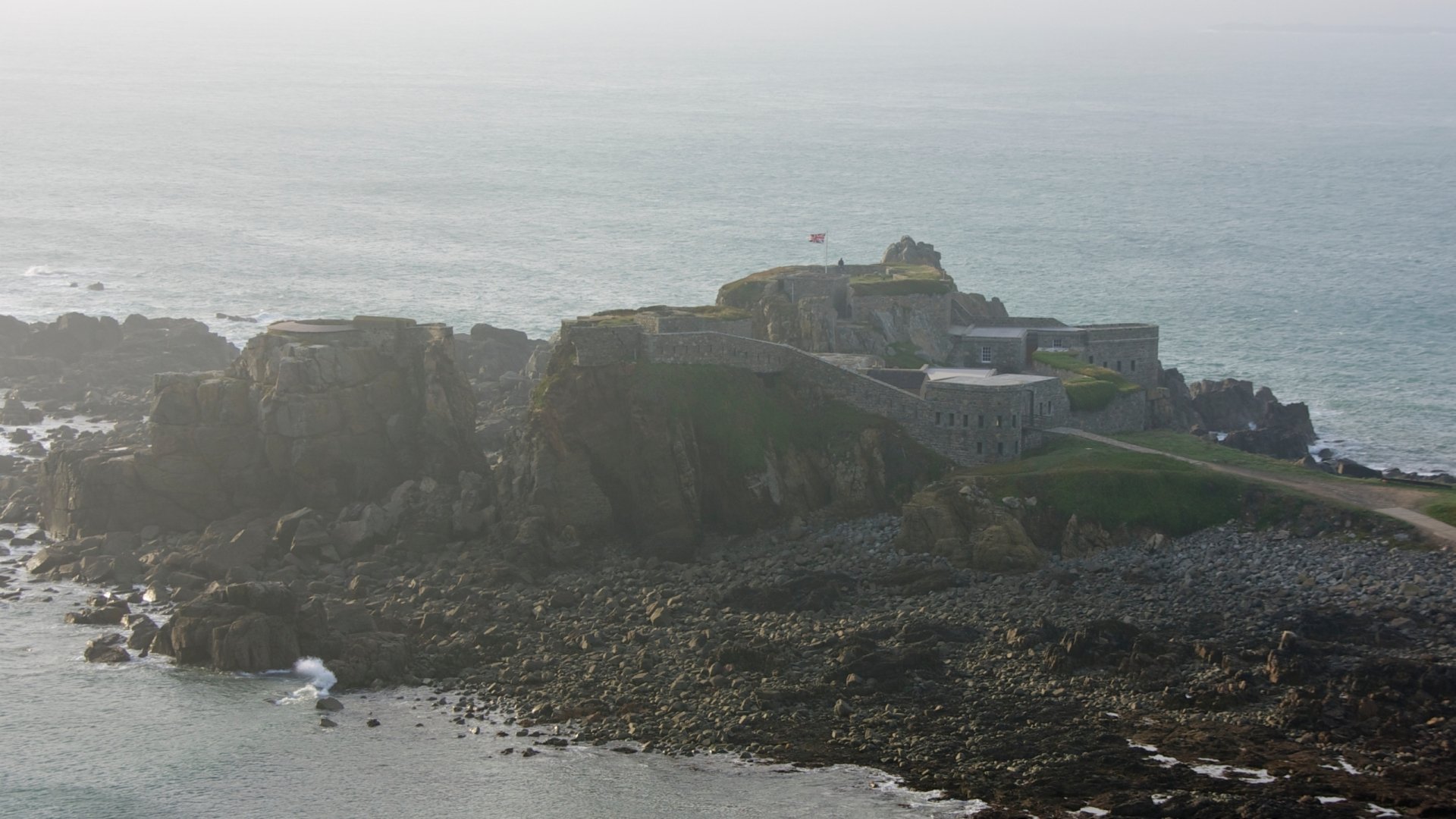 Aerial view of Fort Clonque, a historic man-made structure perched on rocky cliffs, surrounded by the sea, offering a captivating backdrop for a HD PC desktop wallpaper.