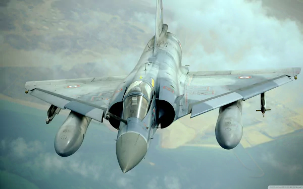 HD desktop wallpaper featuring a Dassault Mirage 2000 military airplane flying above clouds, showcasing its sleek design and powerful presence in the sky.