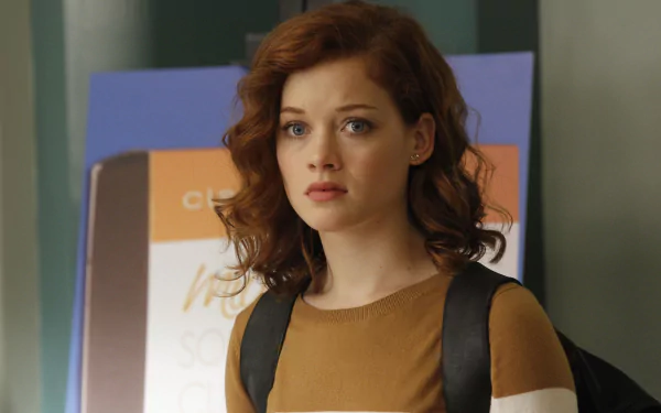 Portrait of a redheaded actress with wavy hair, wearing a brown top and backpack, neutral expression — 2K Quad HD PC desktop wallpaper/background.