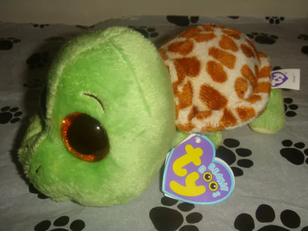 HD desktop wallpaper featuring a man-made Beanie Boos plush turtle with a green head and orange spotted shell on a paw-print patterned surface.