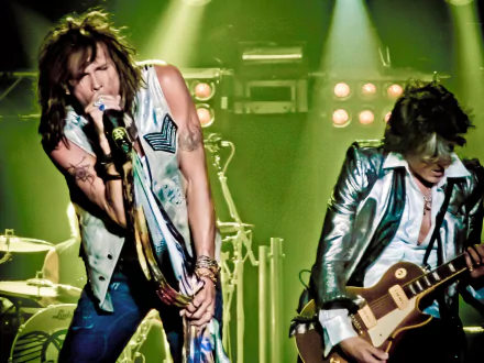 Aerosmith performs energetically on stage, surrounded by vibrant lighting, captured in this HD desktop wallpaper and background, showcasing their iconic rock presence.