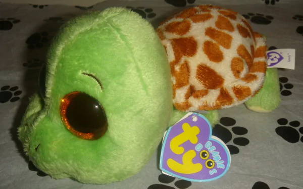 HD desktop wallpaper featuring a man-made Beanie Boos plush turtle with a green head and orange spotted shell on a paw-print patterned surface.