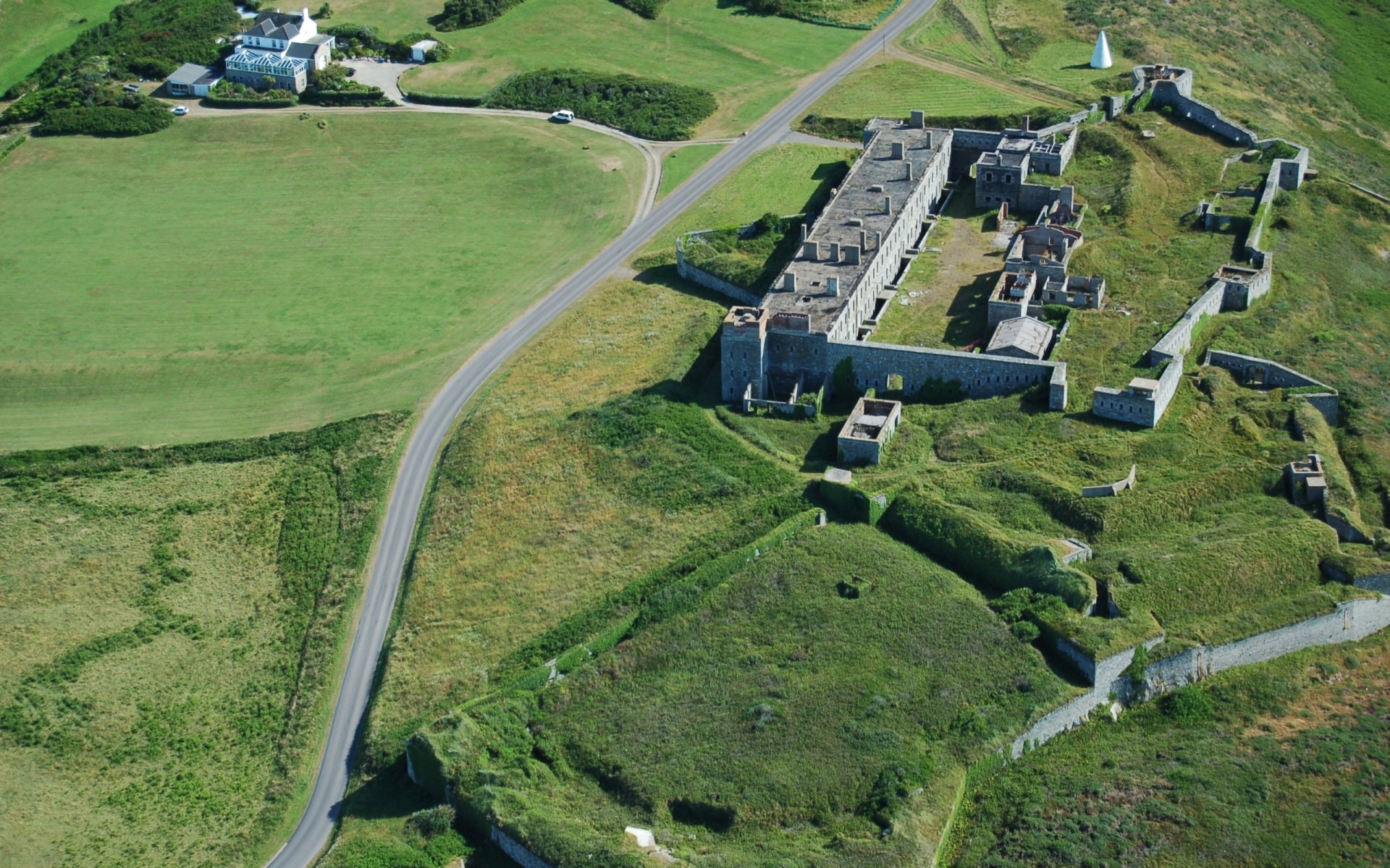 Aerial view of man-made Fort Tourgis on a grassy headland with stone walls and access roads — 2K Quad HD PC desktop wallpaper and background.