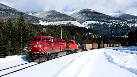 HD desktop wallpaper featuring a red freight train traveling through snowy terrain with forested mountains in the background under a cloudy sky.