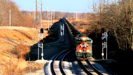 HD desktop wallpaper showcasing a bright orange WP locomotive traveling on curved train tracks through a rural landscape with leafless trees and clear skies.