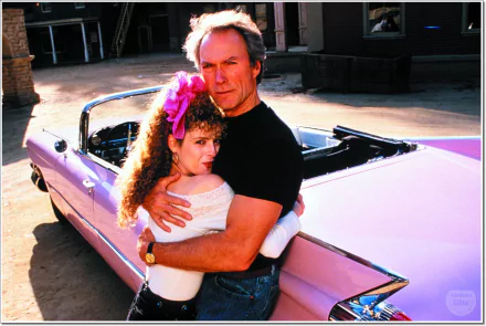 HD movie wallpaper featuring a scene from Pink Cadillac with a man and woman embracing beside a classic pink convertible car.