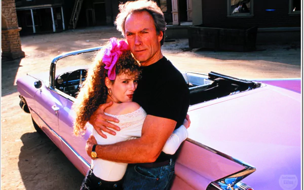 HD movie wallpaper featuring a scene from Pink Cadillac with a man and woman embracing beside a classic pink convertible car.