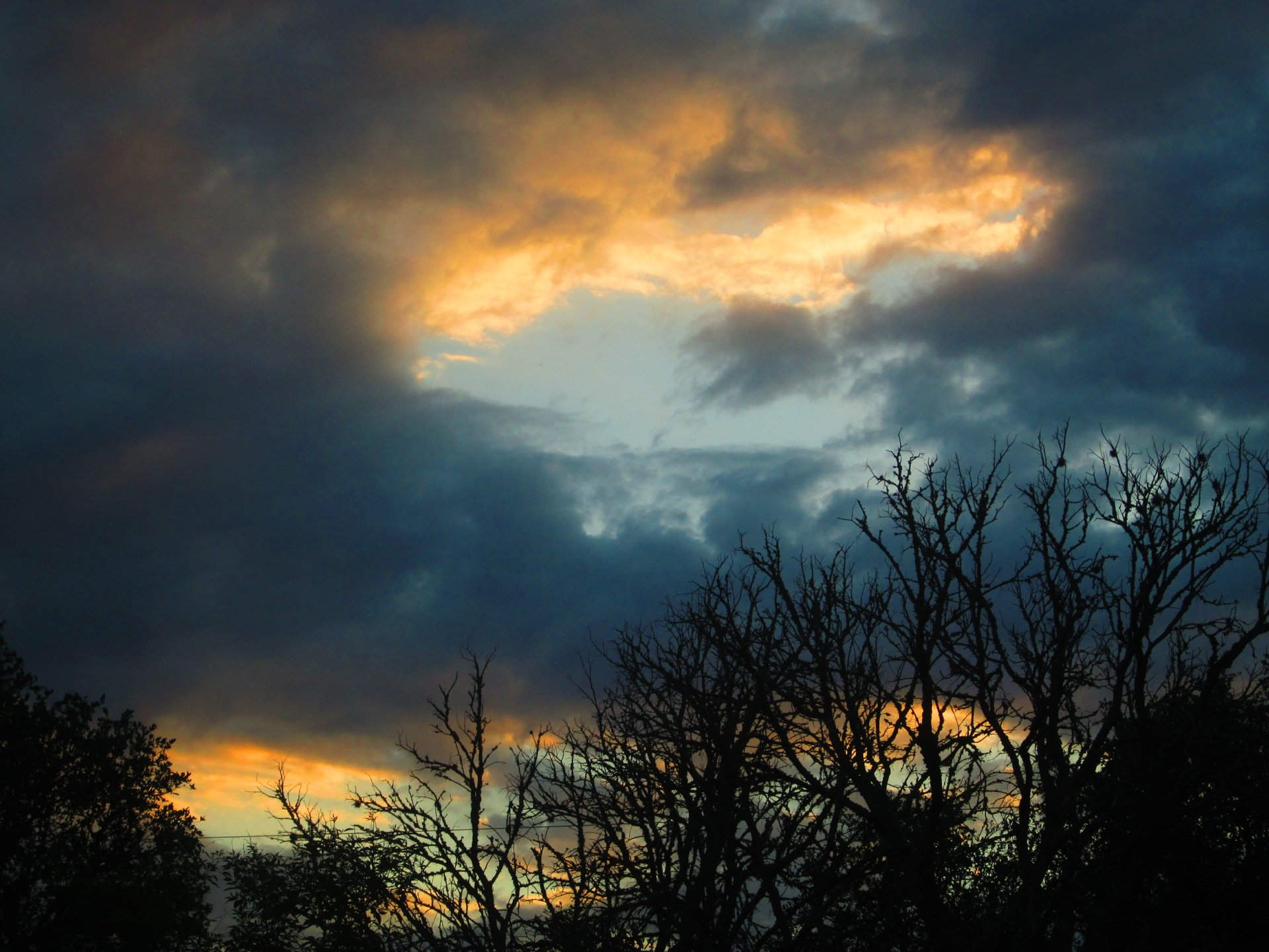 Nature cloud scene at sunset with silhouetted trees and a glowing break in storm clouds — 4K Ultra HD PC desktop wallpaper and background.