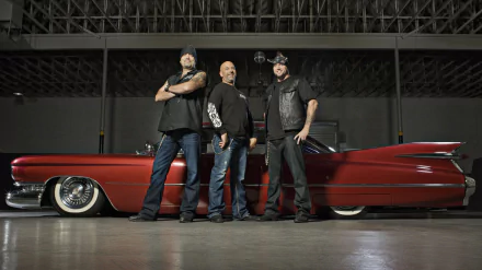 HD desktop wallpaper featuring three men from the TV show Counting Cars standing confidently in front of a classic red lowrider car in a garage setting.