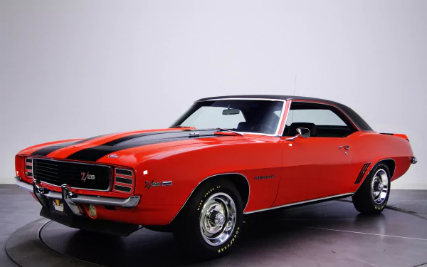 HD PC desktop wallpaper featuring a classic red Chevrolet Camaro Z28 RS muscle car with black racing stripes in a studio setting.