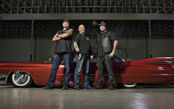HD desktop wallpaper featuring three men from the TV show Counting Cars standing confidently in front of a classic red lowrider car in a garage setting.